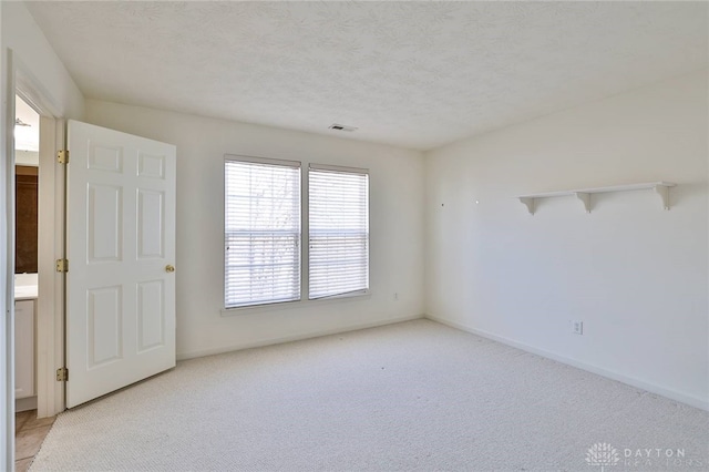 empty room featuring a textured ceiling, baseboards, visible vents, and light colored carpet