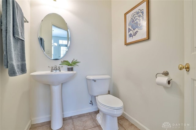 half bath with baseboards, toilet, and tile patterned floors