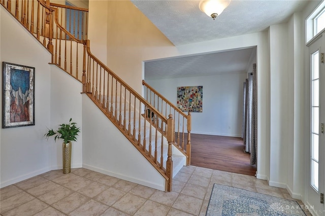 entrance foyer with stairs, a textured ceiling, baseboards, and light tile patterned floors