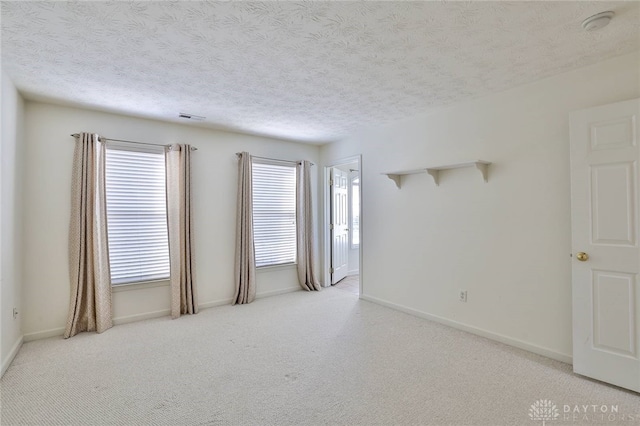 empty room with baseboards, visible vents, a textured ceiling, and light colored carpet