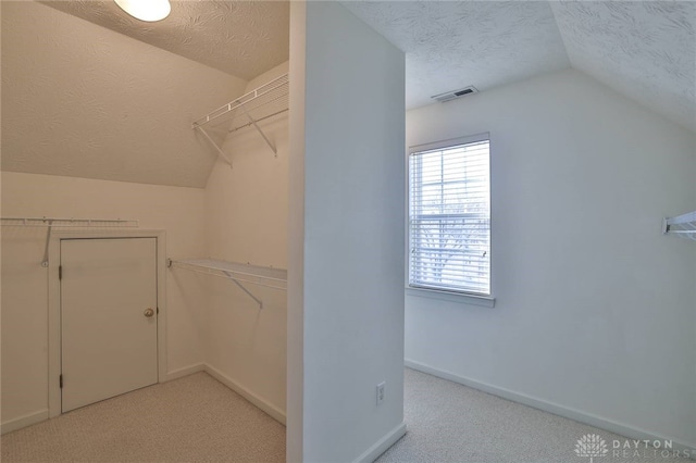 spacious closet with vaulted ceiling, light carpet, and visible vents