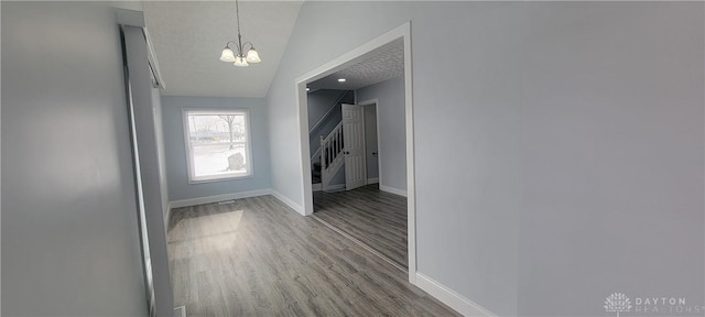 corridor featuring wood-type flooring, a textured ceiling, a notable chandelier, and vaulted ceiling