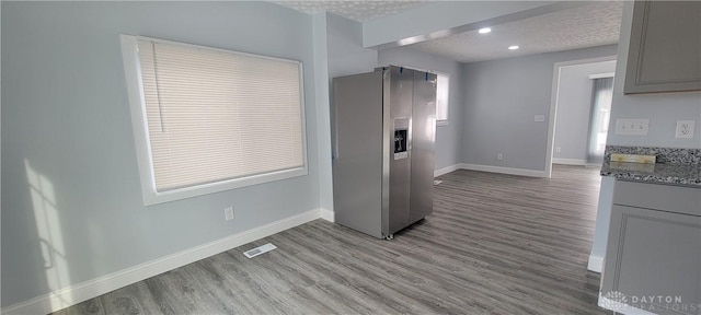 kitchen featuring light hardwood / wood-style floors, gray cabinets, stainless steel refrigerator with ice dispenser, a textured ceiling, and stone counters