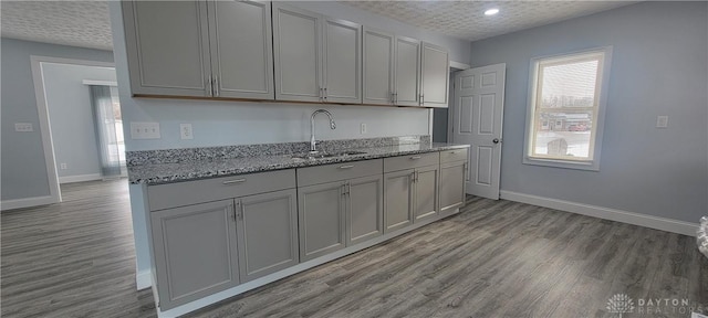 kitchen with gray cabinetry, light stone counters, and sink