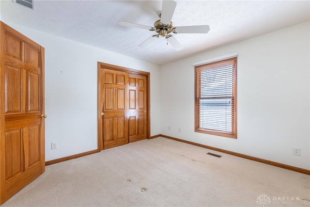 unfurnished bedroom with light carpet, a textured ceiling, and ceiling fan