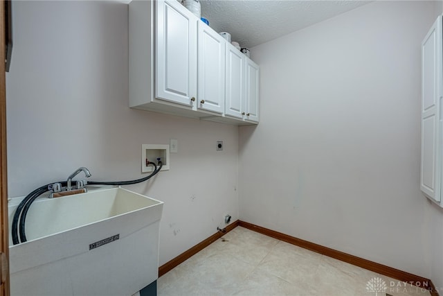 clothes washing area with a textured ceiling, sink, hookup for a washing machine, hookup for an electric dryer, and cabinets