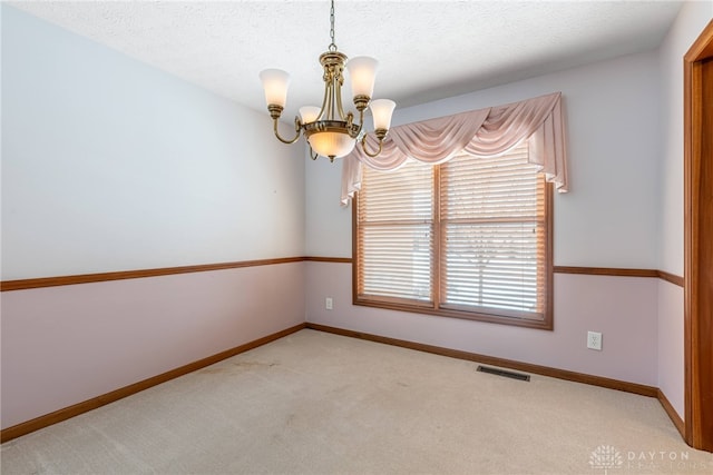 carpeted empty room featuring a textured ceiling and an inviting chandelier