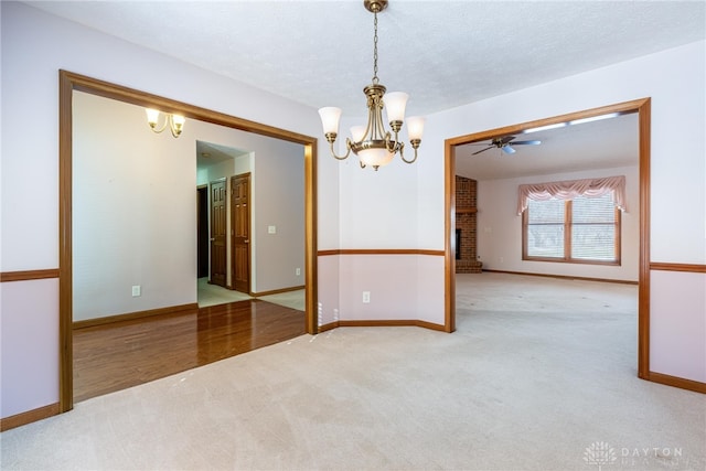 spare room with a brick fireplace, light colored carpet, a textured ceiling, and ceiling fan with notable chandelier