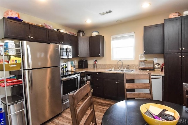 kitchen featuring sink, dark brown cabinets, dark wood-type flooring, stainless steel appliances, and light stone counters