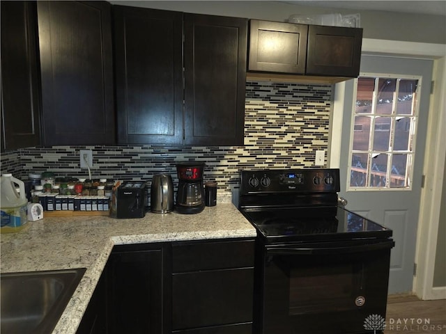 kitchen featuring light stone counters, black electric range oven, sink, and backsplash