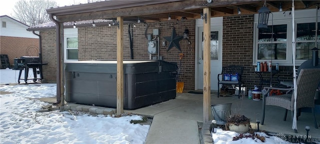 snow covered patio featuring a grill, a hot tub, and a garage