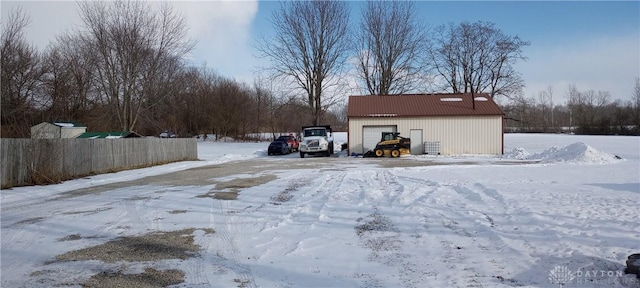 yard layered in snow featuring an outbuilding, a garage, and fence