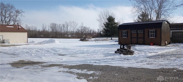 snowy yard featuring a storage unit, a detached garage, and an outdoor structure