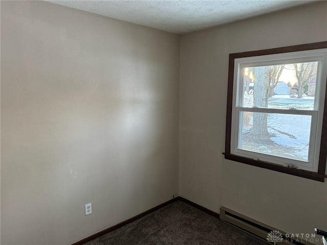 spare room with dark colored carpet, a baseboard radiator, baseboards, and a textured ceiling