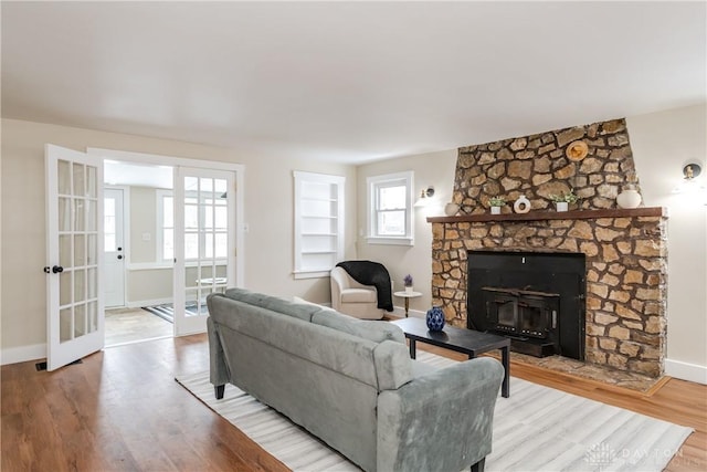 living room featuring hardwood / wood-style flooring, built in shelves, a stone fireplace, and french doors