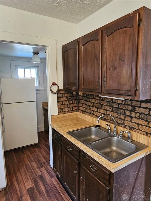 kitchen featuring sink, dark wood-type flooring, white fridge, a textured ceiling, and dark brown cabinetry