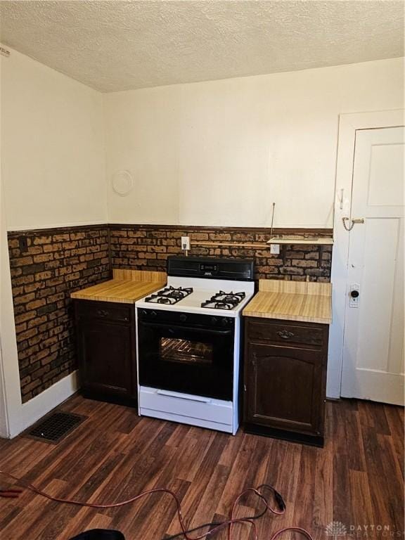 kitchen with gas range oven, a textured ceiling, dark wood-type flooring, and brick wall