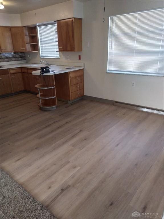 kitchen with brown cabinetry, light countertops, light wood-style flooring, and open shelves