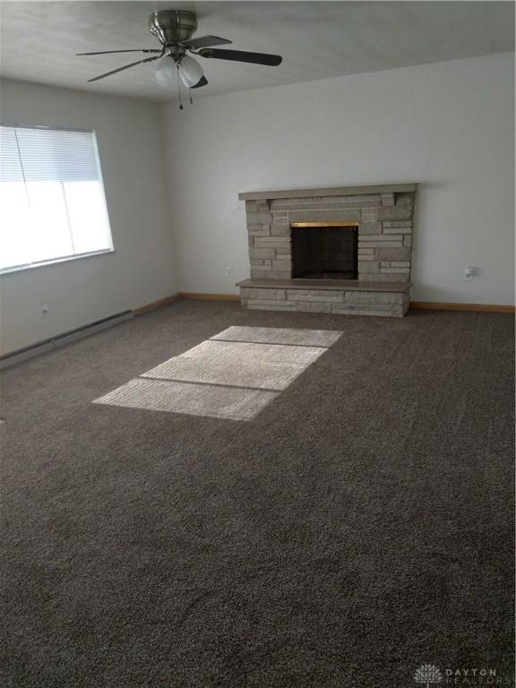 unfurnished living room with ceiling fan, dark carpet, and a fireplace