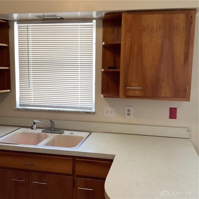 kitchen with open shelves, brown cabinetry, light countertops, and a sink