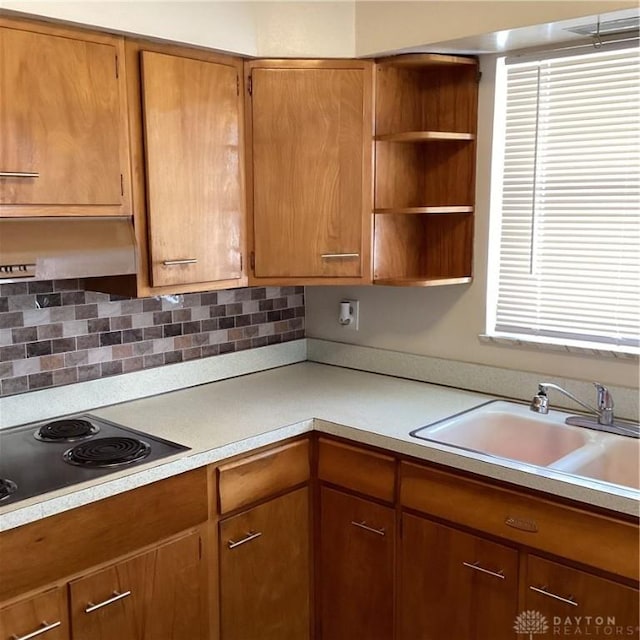 kitchen featuring brown cabinets, black electric cooktop, light countertops, a sink, and exhaust hood