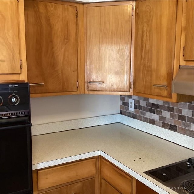 kitchen with brown cabinetry, light countertops, under cabinet range hood, and black appliances