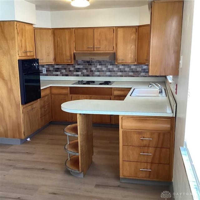 kitchen featuring brown cabinetry, under cabinet range hood, light countertops, black appliances, and a sink