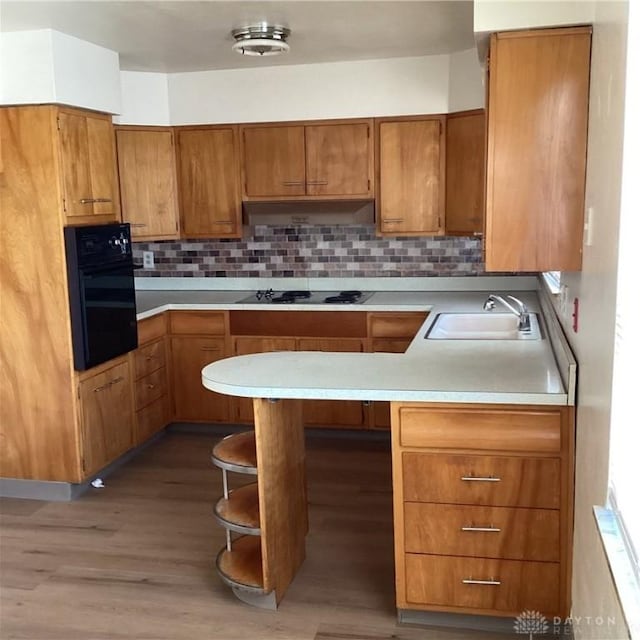 kitchen with under cabinet range hood, a sink, light countertops, brown cabinets, and black appliances