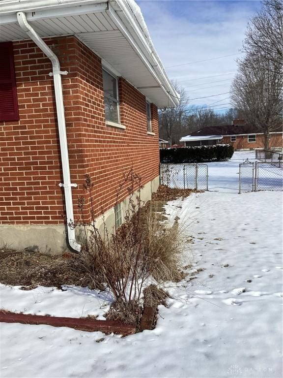 snow covered property featuring brick siding and fence