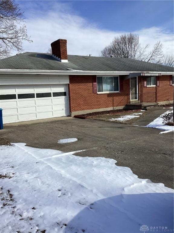 single story home with driveway, brick siding, a chimney, and an attached garage