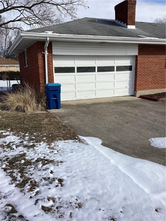 snow covered garage featuring driveway