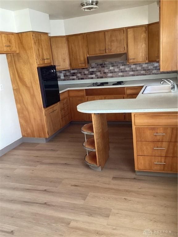 kitchen featuring light countertops, brown cabinetry, a peninsula, under cabinet range hood, and black appliances