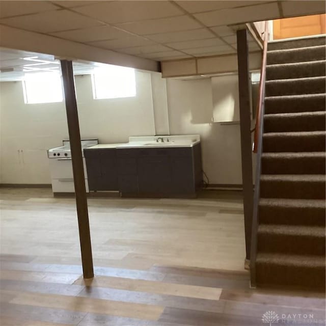 basement with a drop ceiling, a sink, baseboards, stairs, and light wood finished floors