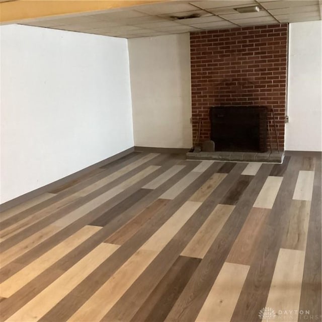 finished basement featuring dark wood-style floors, a paneled ceiling, a brick fireplace, and baseboards