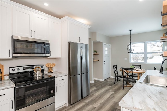 kitchen featuring white cabinets, decorative light fixtures, sink, stainless steel appliances, and light stone counters