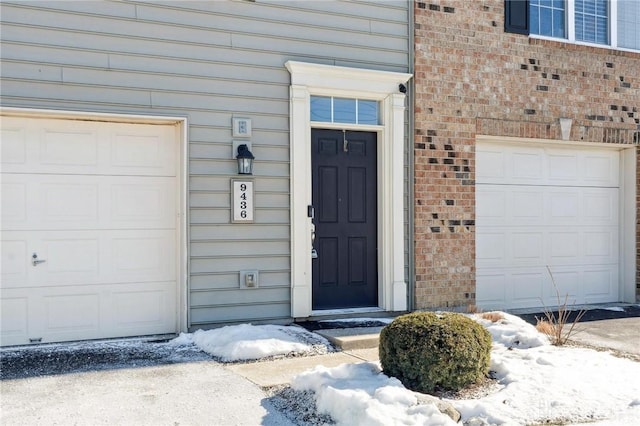 snow covered property entrance featuring a garage