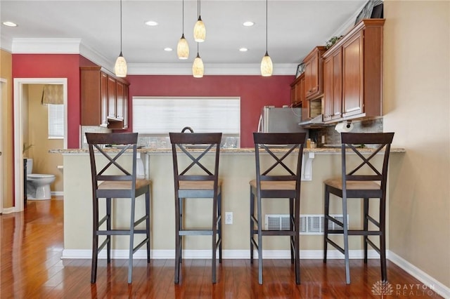 kitchen with dark hardwood / wood-style floors, ornamental molding, light stone countertops, a kitchen bar, and decorative light fixtures