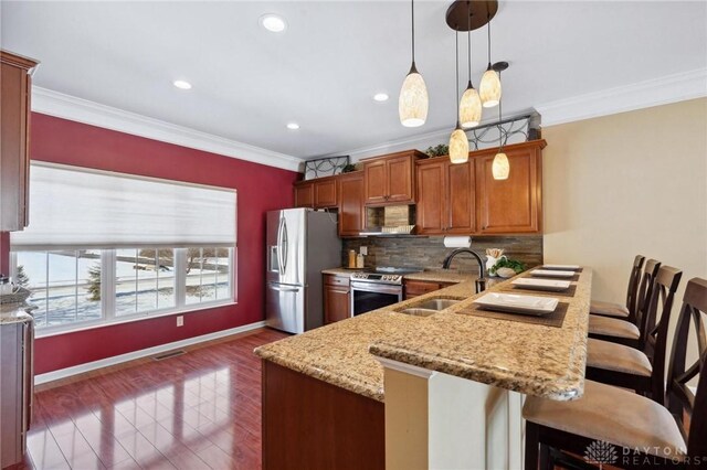 kitchen with sink, appliances with stainless steel finishes, hanging light fixtures, a kitchen breakfast bar, and light stone counters