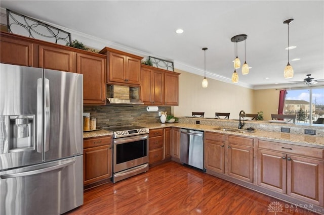 kitchen with appliances with stainless steel finishes, sink, wall chimney range hood, kitchen peninsula, and pendant lighting