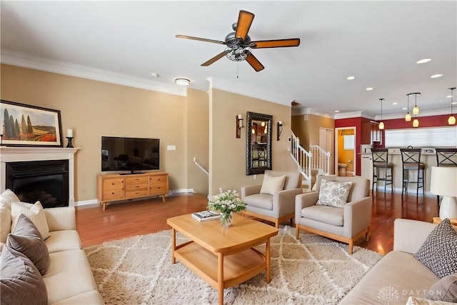 living room with wood-type flooring, ornamental molding, and ceiling fan