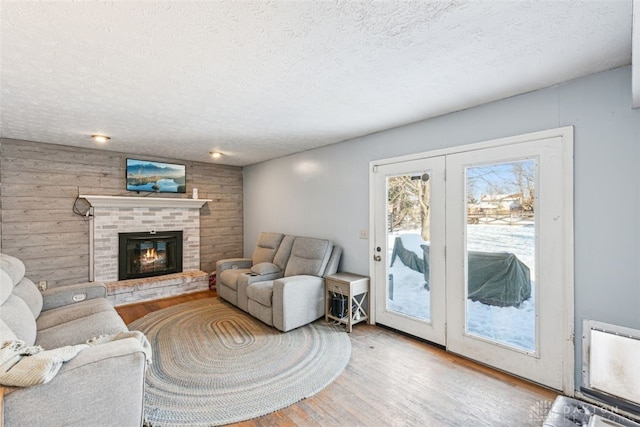 living room featuring a fireplace, light hardwood / wood-style floors, a textured ceiling, and wood walls