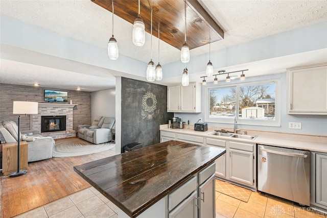 kitchen featuring sink, dishwasher, hanging light fixtures, a fireplace, and light tile patterned flooring