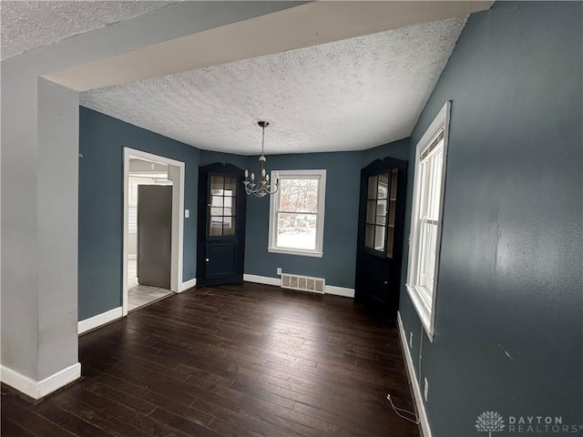 unfurnished dining area featuring an inviting chandelier, dark hardwood / wood-style flooring, and a textured ceiling