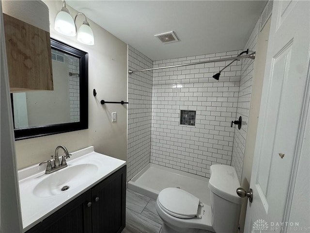 bathroom with vanity, tiled shower, and toilet