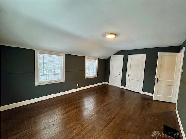 unfurnished bedroom with lofted ceiling, dark hardwood / wood-style flooring, and two closets