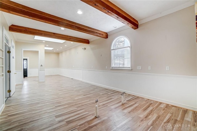 empty room featuring light wood-type flooring, beamed ceiling, a skylight, and ornamental molding