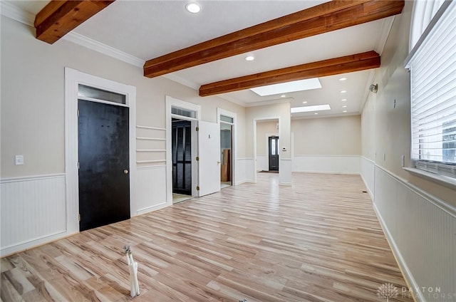 empty room featuring light wood-type flooring, a skylight, and ornamental molding