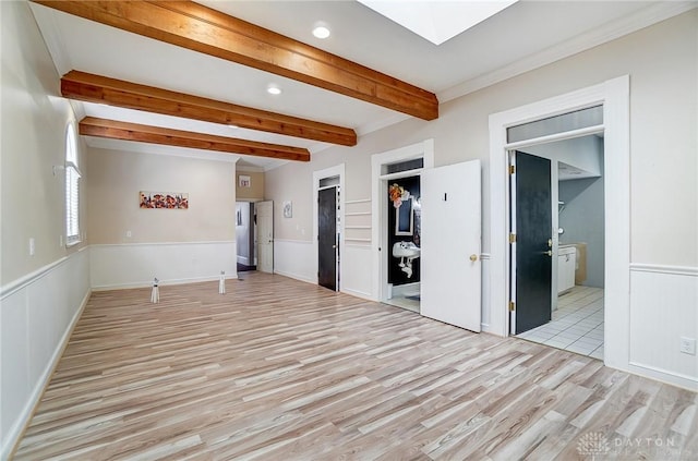 empty room with a skylight, beam ceiling, and light hardwood / wood-style floors