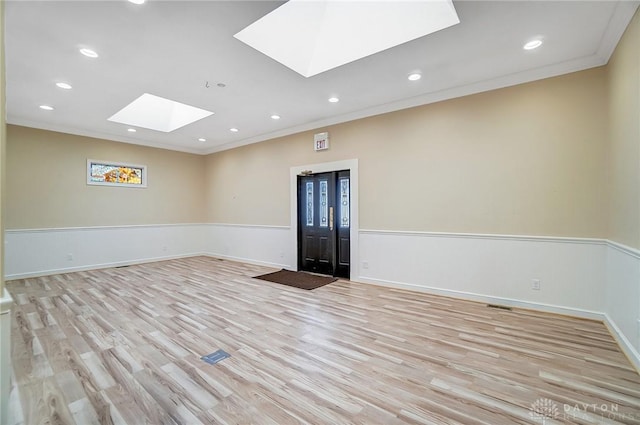 empty room with a skylight, crown molding, and light hardwood / wood-style floors