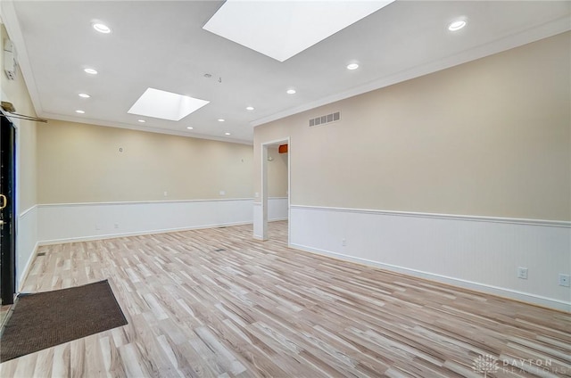 empty room featuring a skylight, light hardwood / wood-style flooring, and crown molding